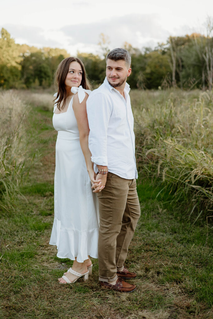 Engaged couple standing back to back holding hands at Waveny Park in New Canaan, Connecticut