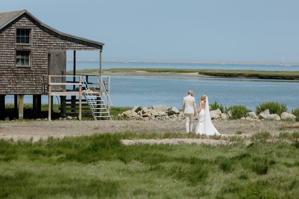 Bride & Groom holding hands, walking in the distance near the ocean for wedding portraits in Duxbury, MA.