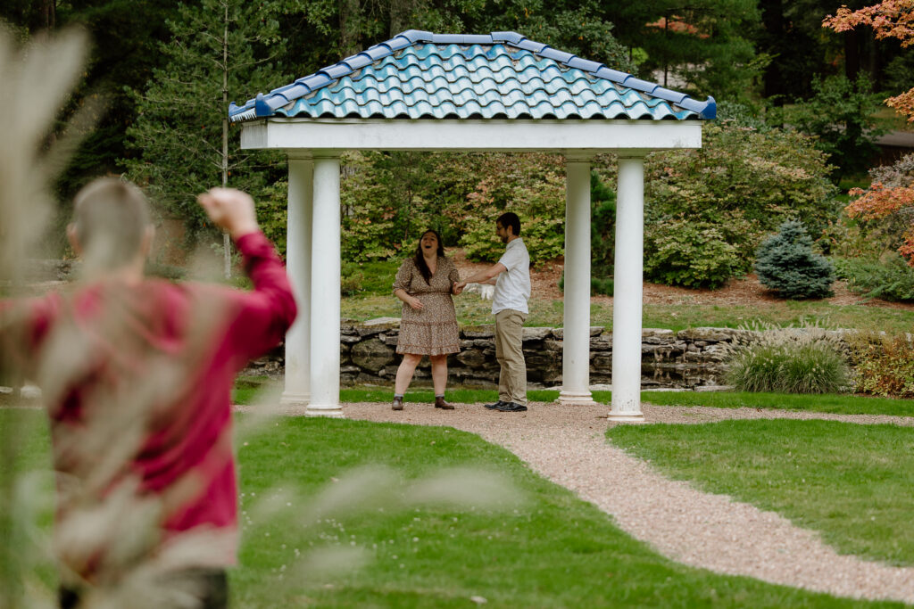 Connecticut proposal, bride and groom just got engaged and family members are running out of the bushes to surprise the couple.