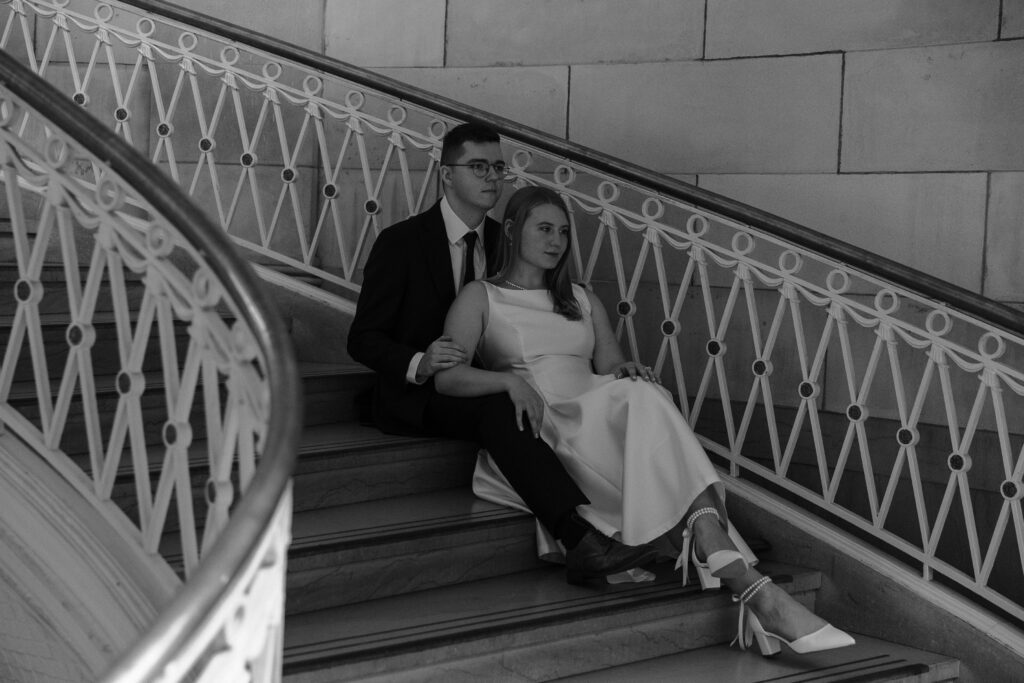 A couple sitting together on the steps inside Hartford City Hall for their romantic engagement session.