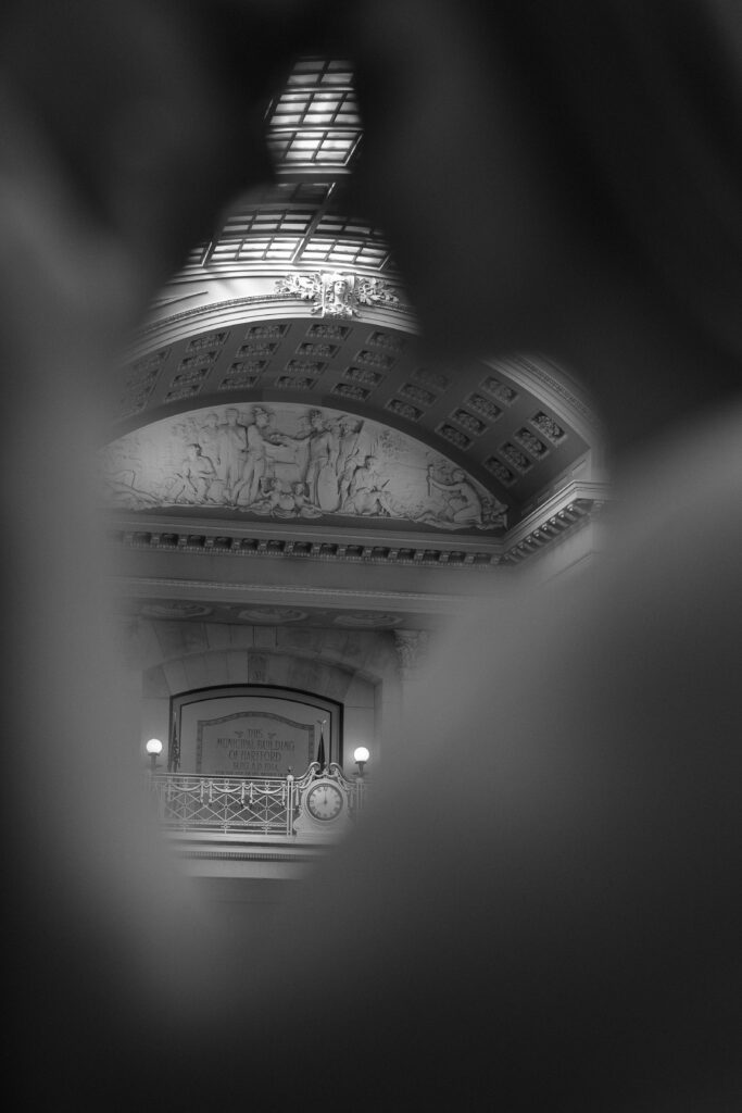 Looking through the view of a couple standing together in Hartford City Hall for their romantic engagement session.