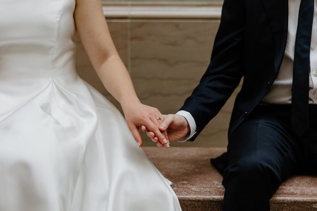 A couple holding hands and sitting on a bench inside Hartford City Hall for their romantic engagement session.