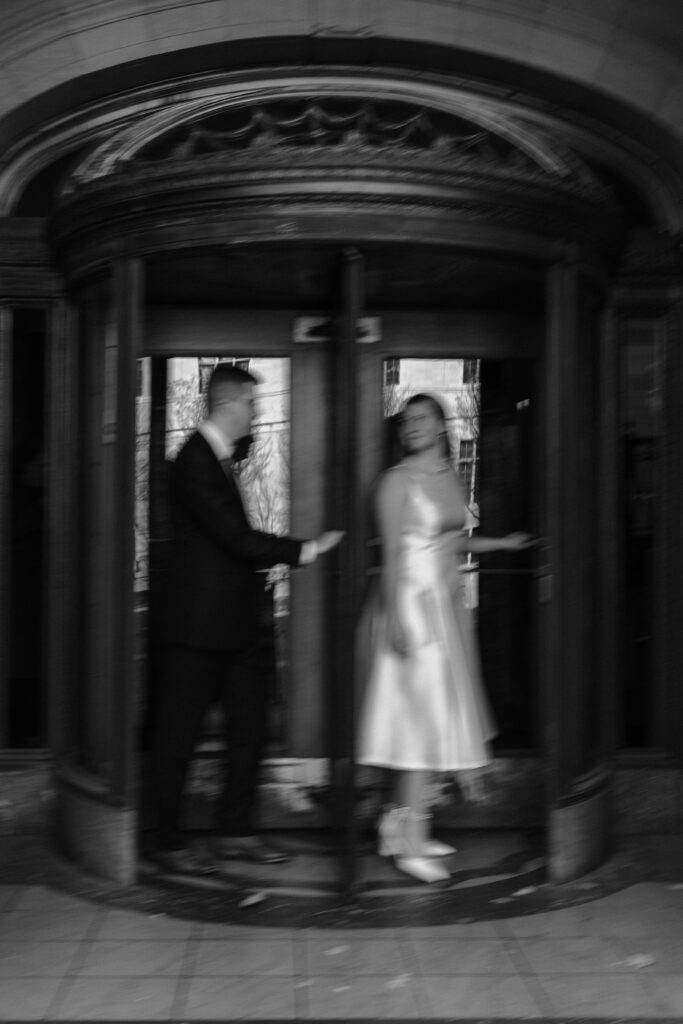 A couple walking around a spinning door outside of Hartford City Hall for their romantic engagement session.