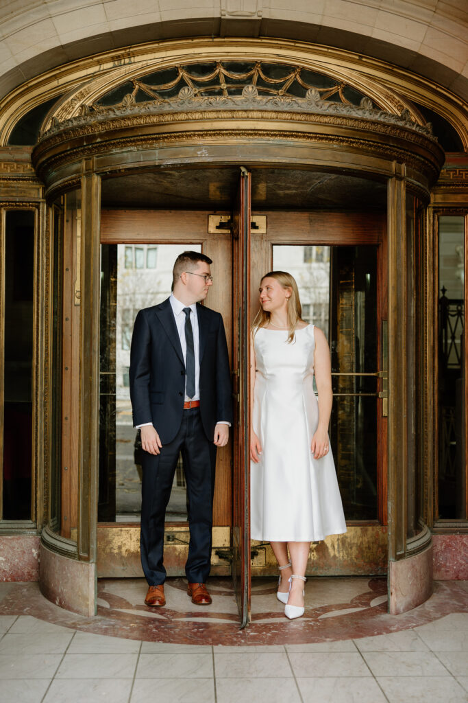 A couple standing in a spinning door outside of Hartford City Hall for their romantic engagement session.