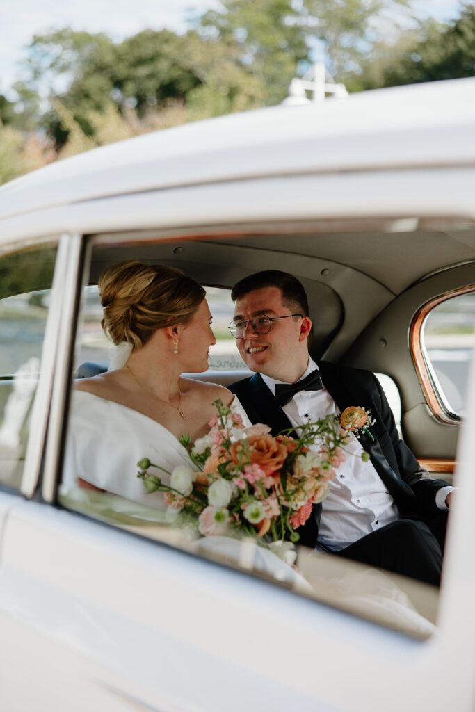Clara and Matt share an intimate, candid moment inside a vintage white car while holding their bouquets on their Curry Estate wedding day.