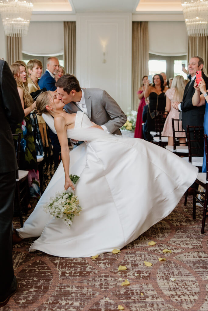 Groom dipping his bride for a kiss in the aisle as guests cheer