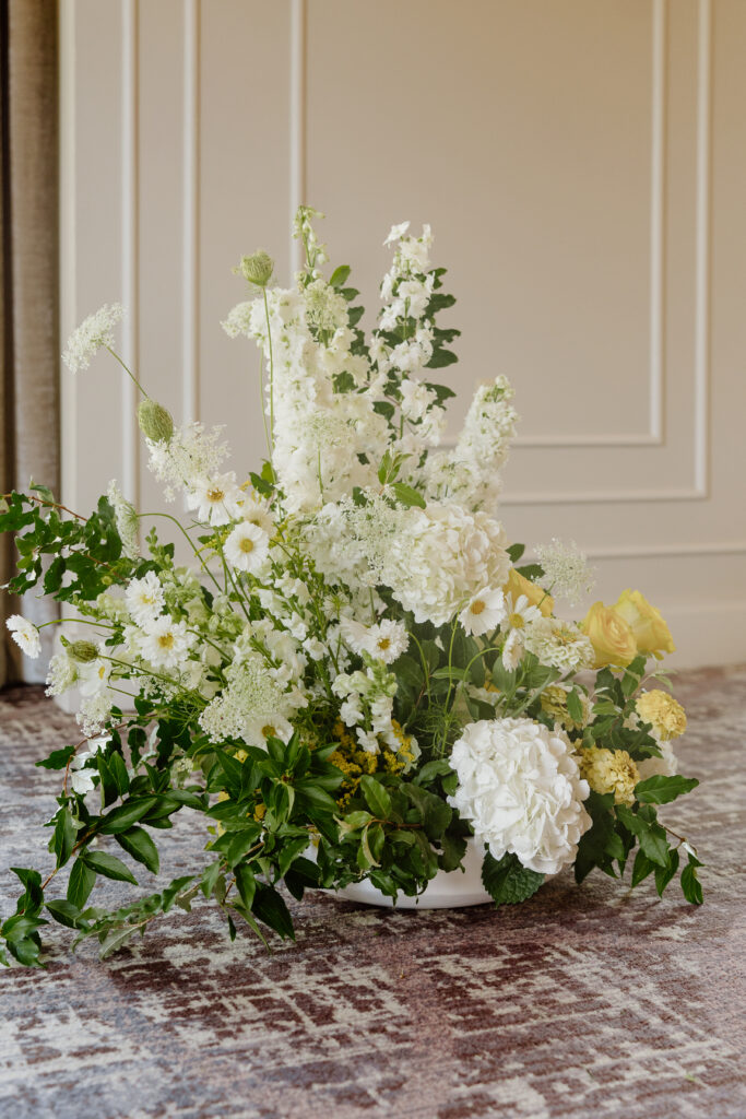 Garden-style ceremony arrangement of white hydrangea, delphinium, and butter yellow roses