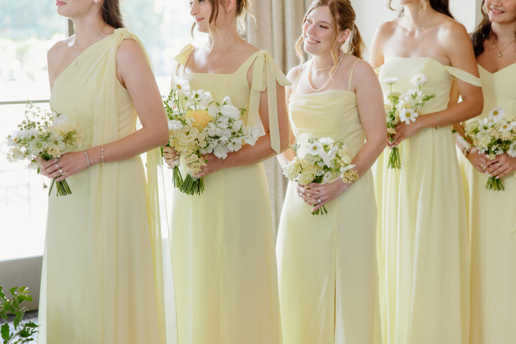 Bridesmaids in butter yellow dresses holding white and yellow bouquets during the ceremony