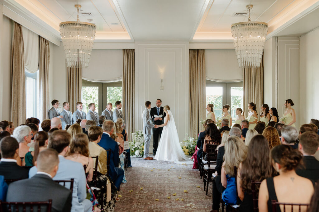 Wide view of a ballroom wedding ceremony with white paneled walls and tall windows