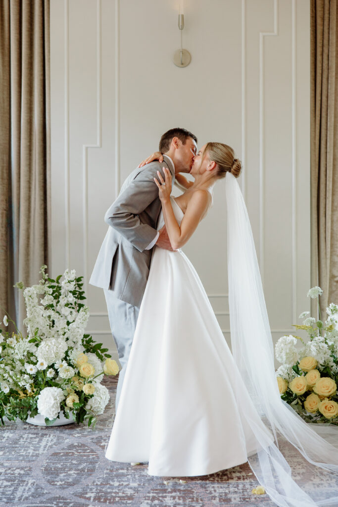 Bride and groom's first kiss at the altar between two garden-style floral arrangements