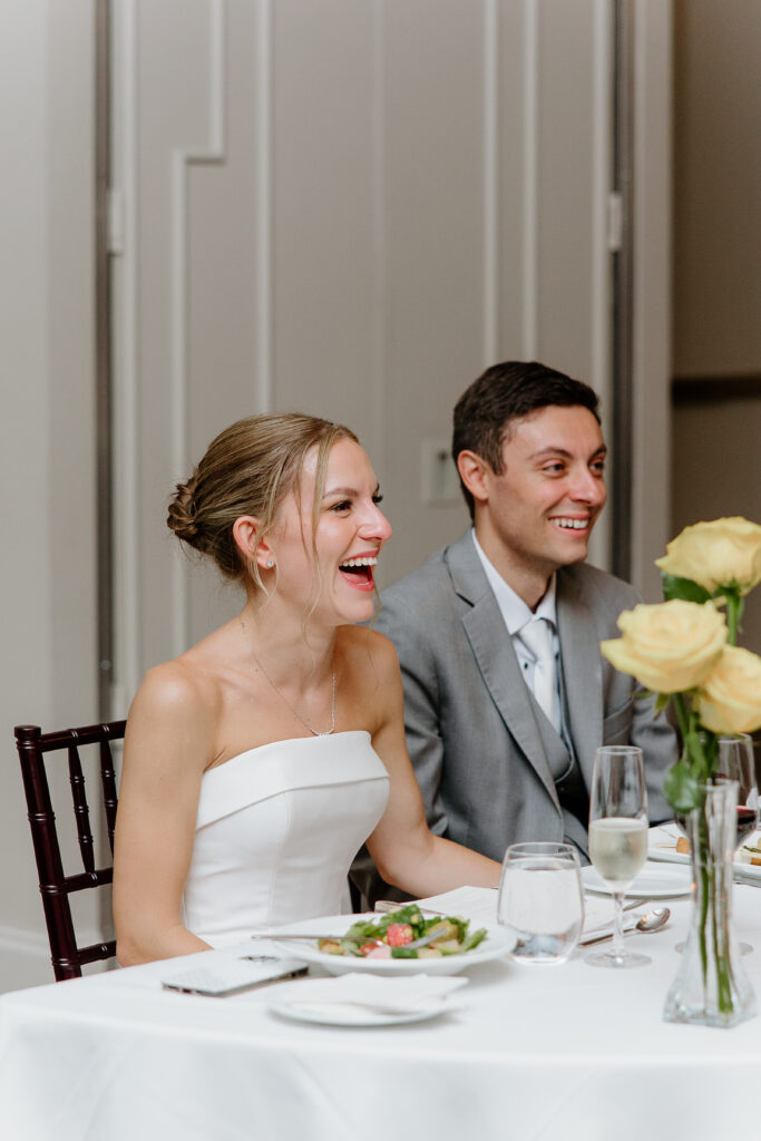 Bride and groom laughing at the sweetheart table during wedding speeches