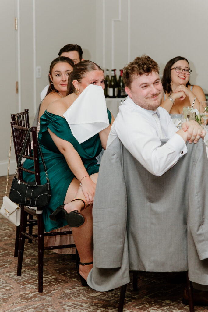 Wedding guests laughing and wiping tears with napkins during the toasts