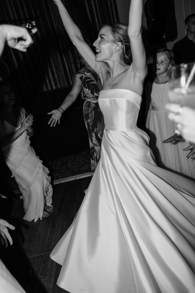 Black and white photo of the bride dancing with her arms in the air