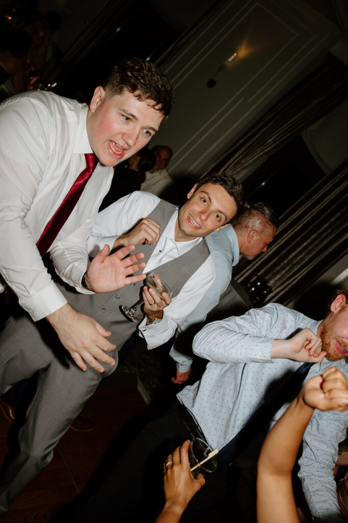 Groomsmen with loosened ties singing and dancing at the reception