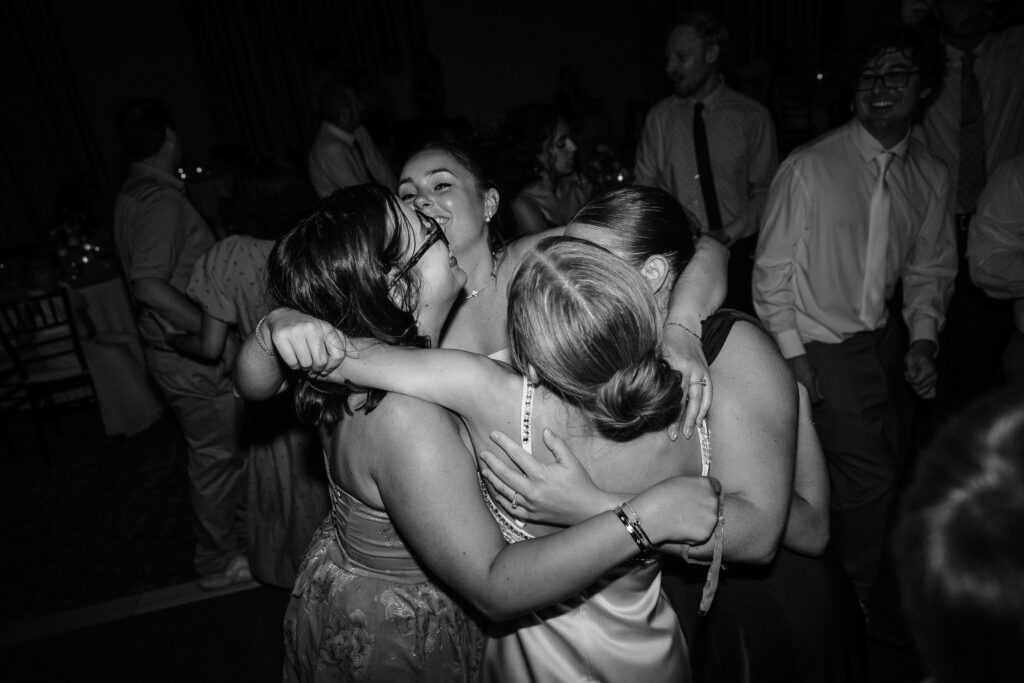 Black and white photo of friends hugging on the dance floor at the end of the night