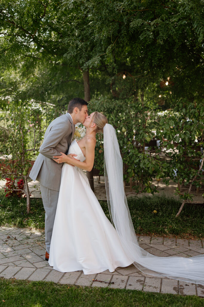 Groom dipping his bride for a kiss after their first look, her long veil trailing on the path