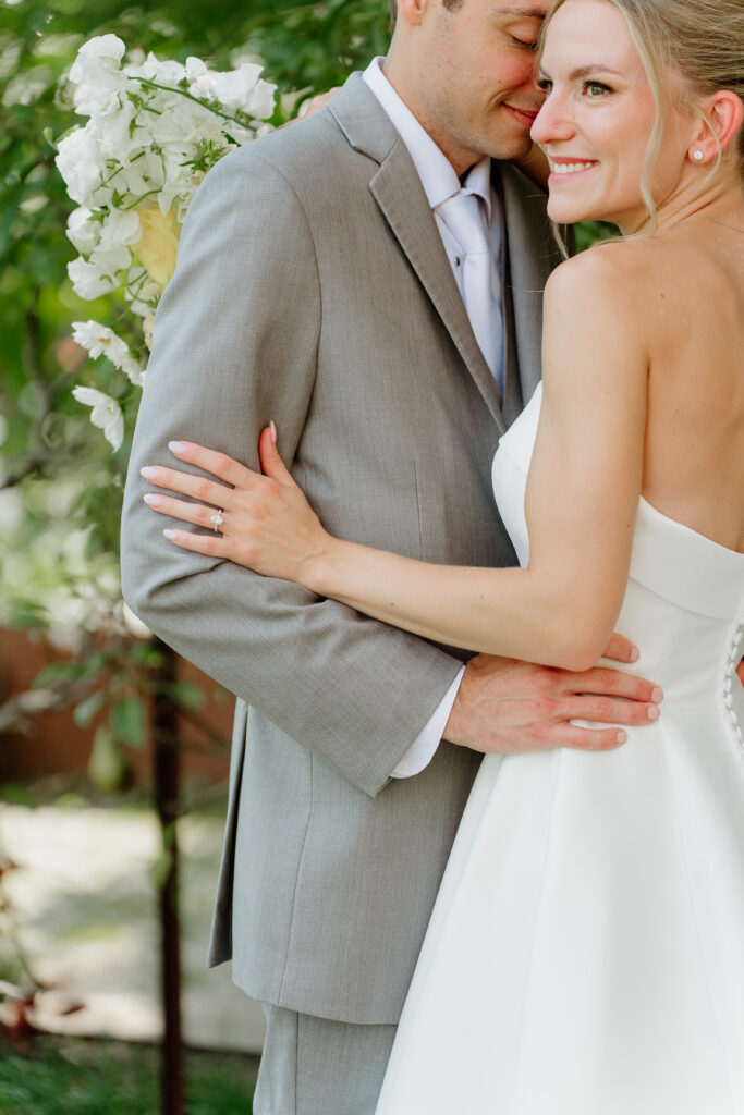 Groom nuzzling the bride's cheek as she hugs his arm, her engagement ring in view