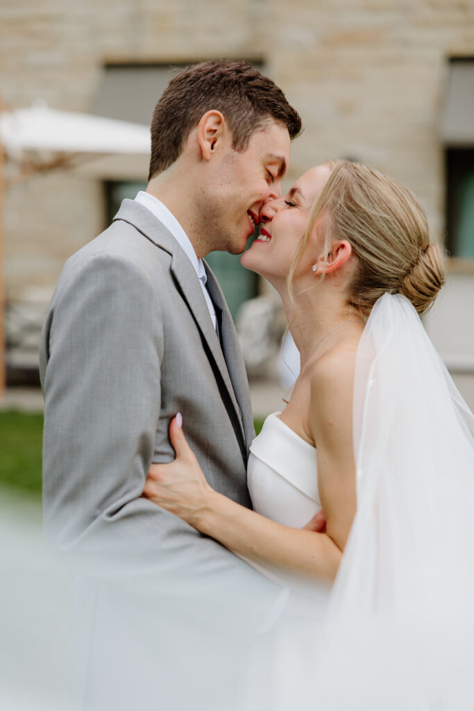 Bride and groom laughing mid-kiss on the back lawn during golden hour portraits
