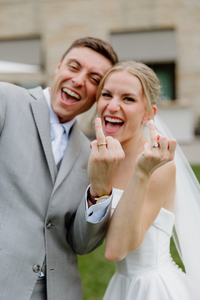 Laughing bride and groom showing off their new wedding rings to the camera
