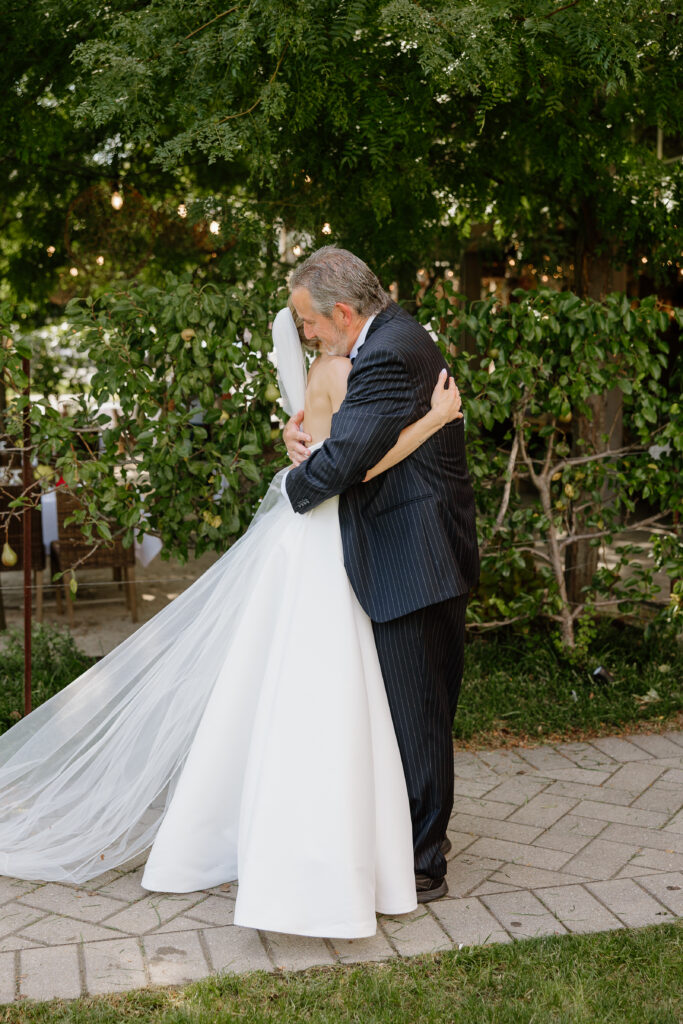 Father of the bride hugging his daughter tightly on the garden path
