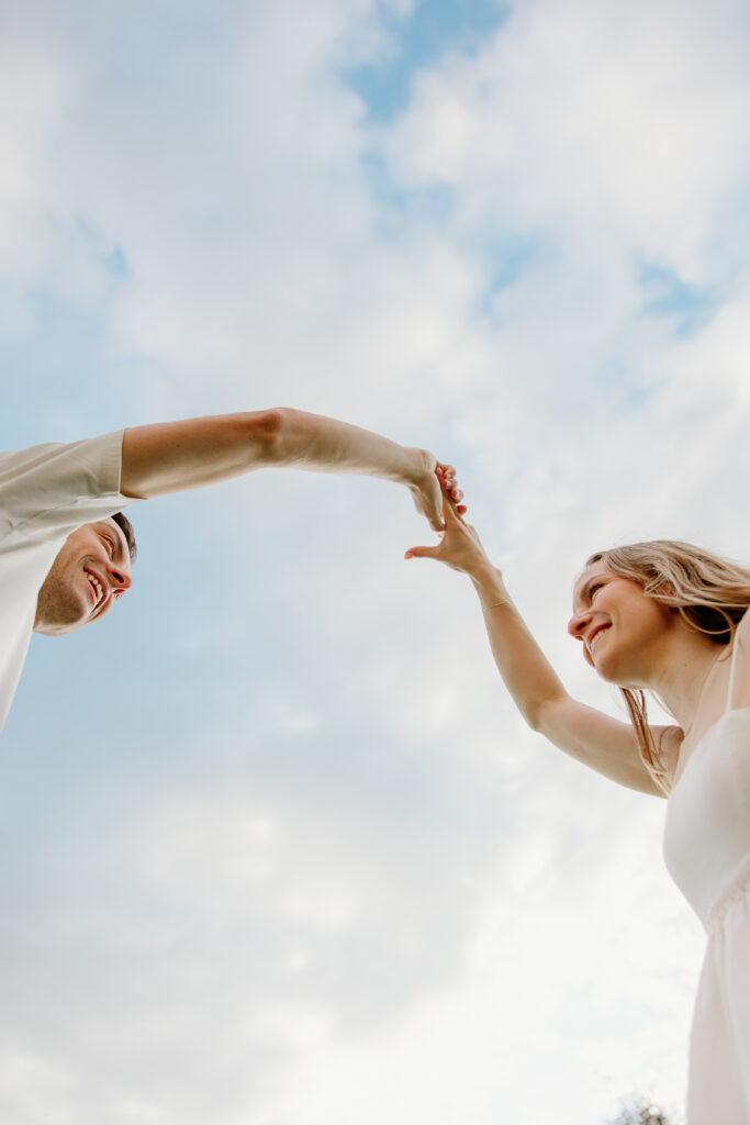 Low-angle shot of a man twirling his fiancée against a blue sky during a Connecticut engagement session